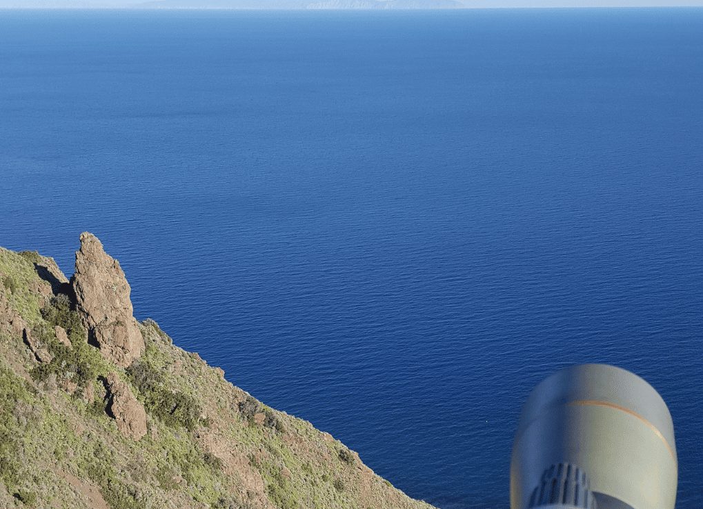 Biologist Alisa Samuelson surveying a shrike nest on the far canyon slope with cliffside and blue ocean view on San Clemente Island.