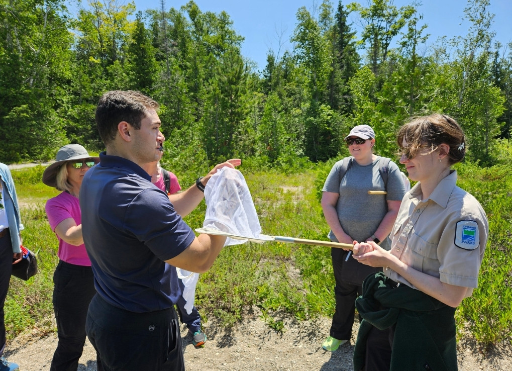 Cole Blair, the lead biologist of WPC’s Native Pollinator Initiative, helps a program participant move a bumble bee from an insect net to a vial. Other participants watch in the background.