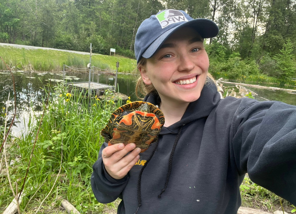 Aysha holding a western painted turtle with a green nature background